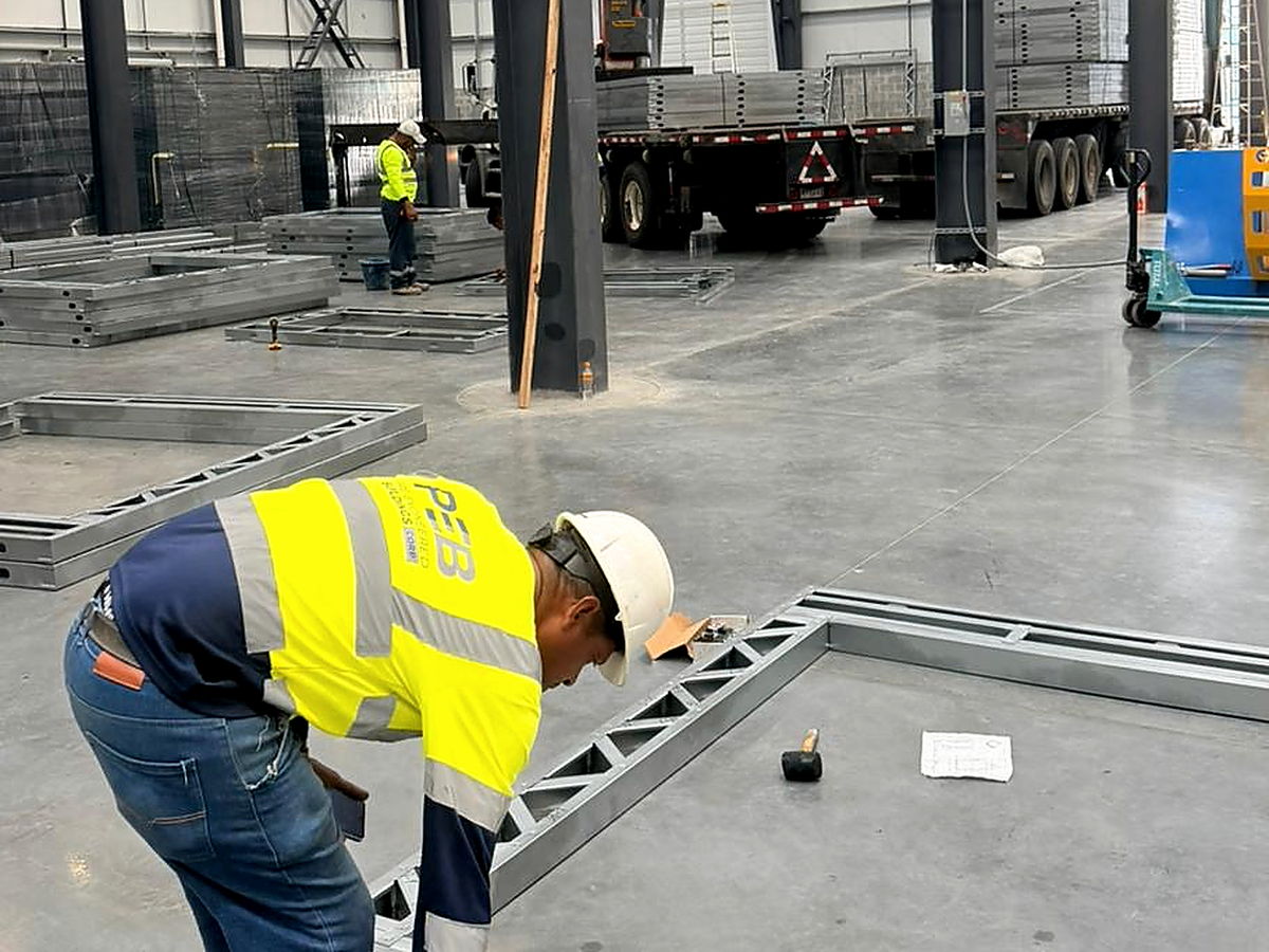 Operario verificando el armado y las escuadras de un marco estructural de acero liviano contra el plano de taller, en la planta de NewCon Steel
