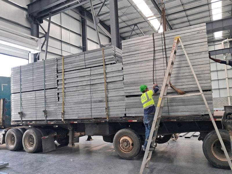 Operario guiando con grúa la carga de estibas de paneles estructurales de acero liviano sobre una plataforma dentro de la planta