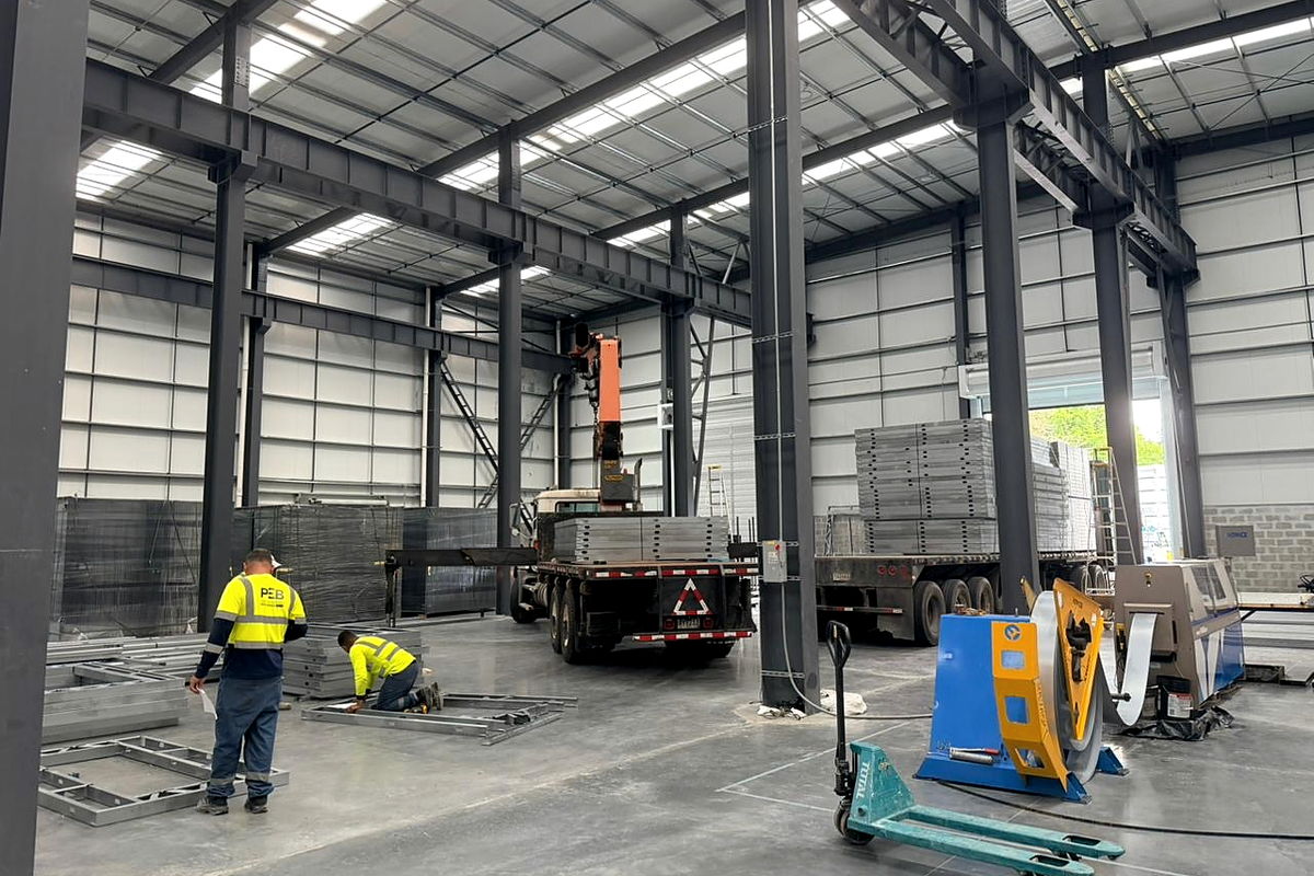 Nave de producción de NewCon Steel: puente grúa, desenrollador de bobina y plataformas cargadas con paneles de acero liviano
