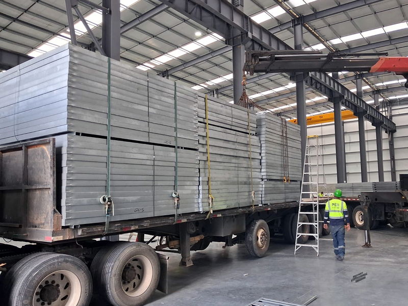 Estibas de paneles estructurales de acero liviano trincadas sobre plataforma, identificadas por lote dentro de la nave